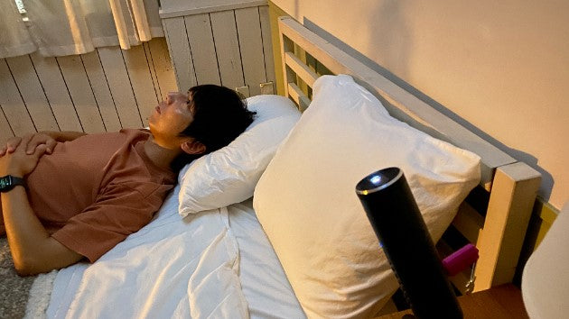 プロジェクターを天井へ向けて設置し、ベッドに寝転んで映像を観ている人